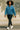 Woman wearing a blue denim jacket and black pants walking on a street.