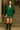 Front view of model in green hoodie with sequin sleeves and pleated skirt on stone staircase