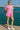 Woman in pink colorblock romper with green trim and white sneakers, standing by marina with yachts