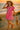Walking on sand in pink mini polo dress with straw hat and red sandals, beach at golden sunset