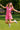 Jumping in park in pink mini polo dress with rainbow sneakers and colorful bracelets, daytime sun