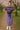 Woman in a plaid shirt and purple skirt standing in a park with cherry blossom trees.