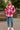Woman in Plaid Fleece Shacket with blue jeans and white sneakers, standing near park bench in city square