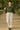 Woman walking in plaid ruffle blouse with ivory trousers and loafers, shaded park walkway.