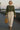 Woman strolling in plaid ruffle blouse with cream maxi skirt and sandals, riverside evening light.