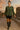 Model walking in plaid ruffle collar blouse with black biker shorts, stone ruins sunset glow.