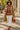 Woman in a plaid shirt and tan coat holding a coffee cup on a sidewalk.