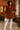 Model standing in cafe in red-brown corduroy mini dress with white tights, knee-high boots, and round bag, warm light