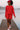 Woman in ruby ribbed outfit with red cap and sneakers, walking on pier over misty lake at sunrise