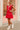 Woman in a red dress standing in front of a pink building