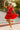 Woman in a red dress with white trim dancing outdoors with balloons in the background