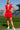 Woman in a red dress standing on a sports field with stadium seats in the background