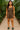 Woman wearing leopard print tie-strap romper with green clogs, walking inside lush botanical conservatory
