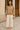 Woman in tan striped sweater and white wide-leg pants with heels on stone city street