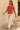 Woman wearing a red and white striped sleeveless top and white pants, standing against a beige wall.