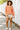 Woman wearing an orange and white striped sweater with white shorts standing on a sidewalk.