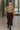 Model walking in taupe textured knit V-neck top with plum midi skirt and lace-up boots, office hallway.