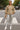 Woman crossing street in taupe textured knit V-neck top with silver leggings and white boots, city setting.