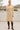 Woman wearing a beige sweater dress and brown knee-high boots standing on a wooden deck.
