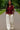 Model walking in maroon zip front vest with wide-leg pants and sneakers, green park pathway daylight.