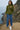 Woman in zip sweater jacket with high neck in Olive Green, near ocean cliff, cloudy sky background